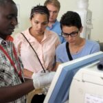Five people observe a gloved man operating medical equipment in a clinic.