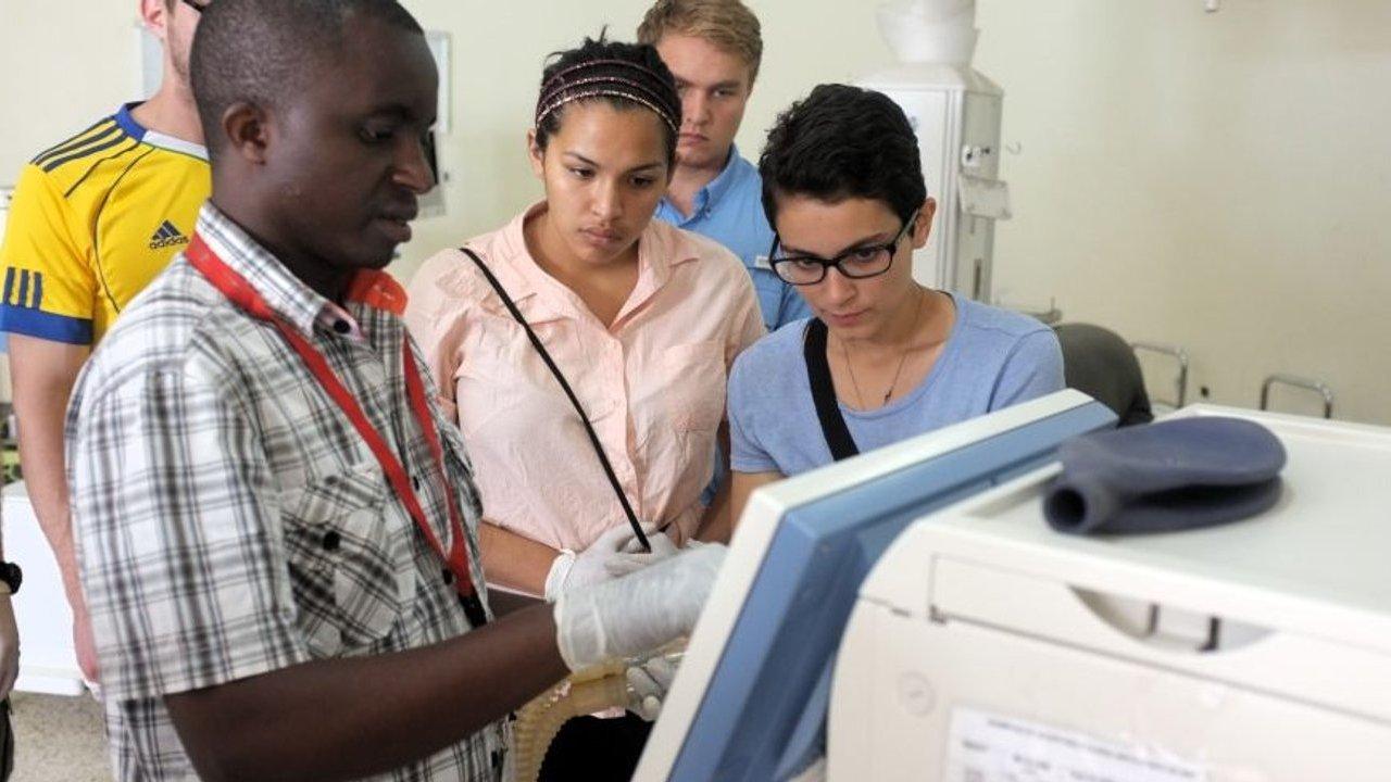 Five people observe a gloved man operating medical equipment in a clinic.