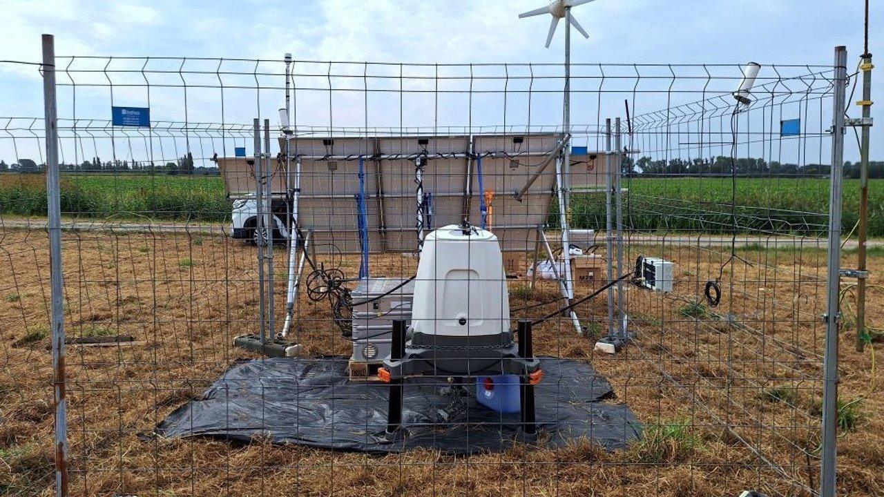 Lidar unit in a fenced field enclosure with solar panels, cables and a small wind turbine