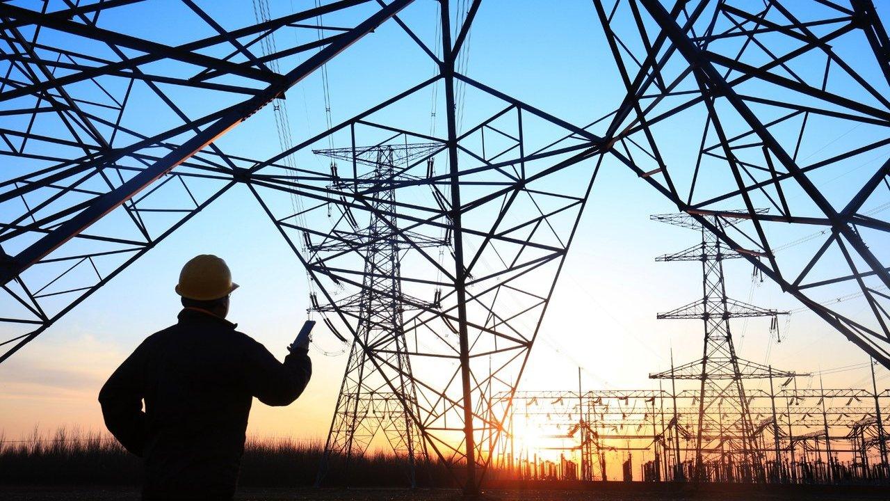 Worker in a hard hat inspecting high-voltage transmission towers and a substation at sunset