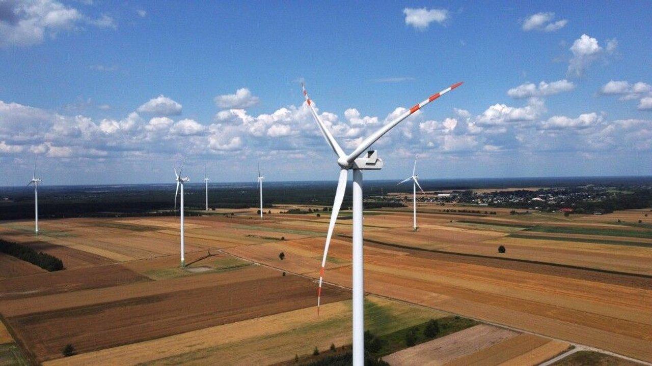 Wind turbines across patchwork farmland under a blue sky with scattered clouds