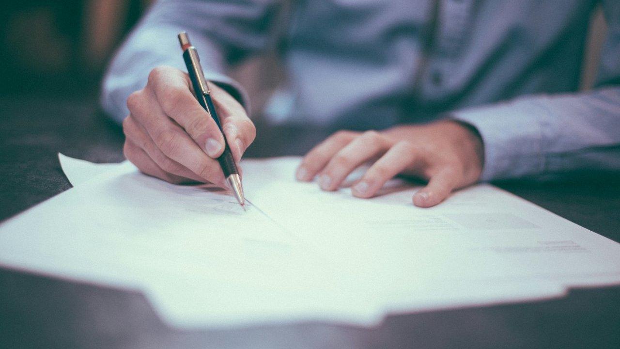 Person signing a document with a pen at a desk