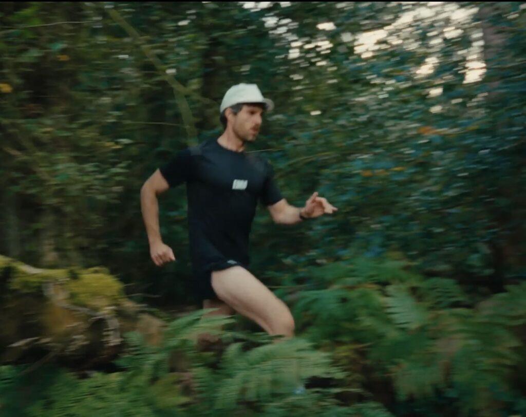 Runner in black sportswear and white cap moving through a leafy woodland.