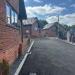 New red-brick houses beside a freshly paved driveway under a blue sky with clouds.
