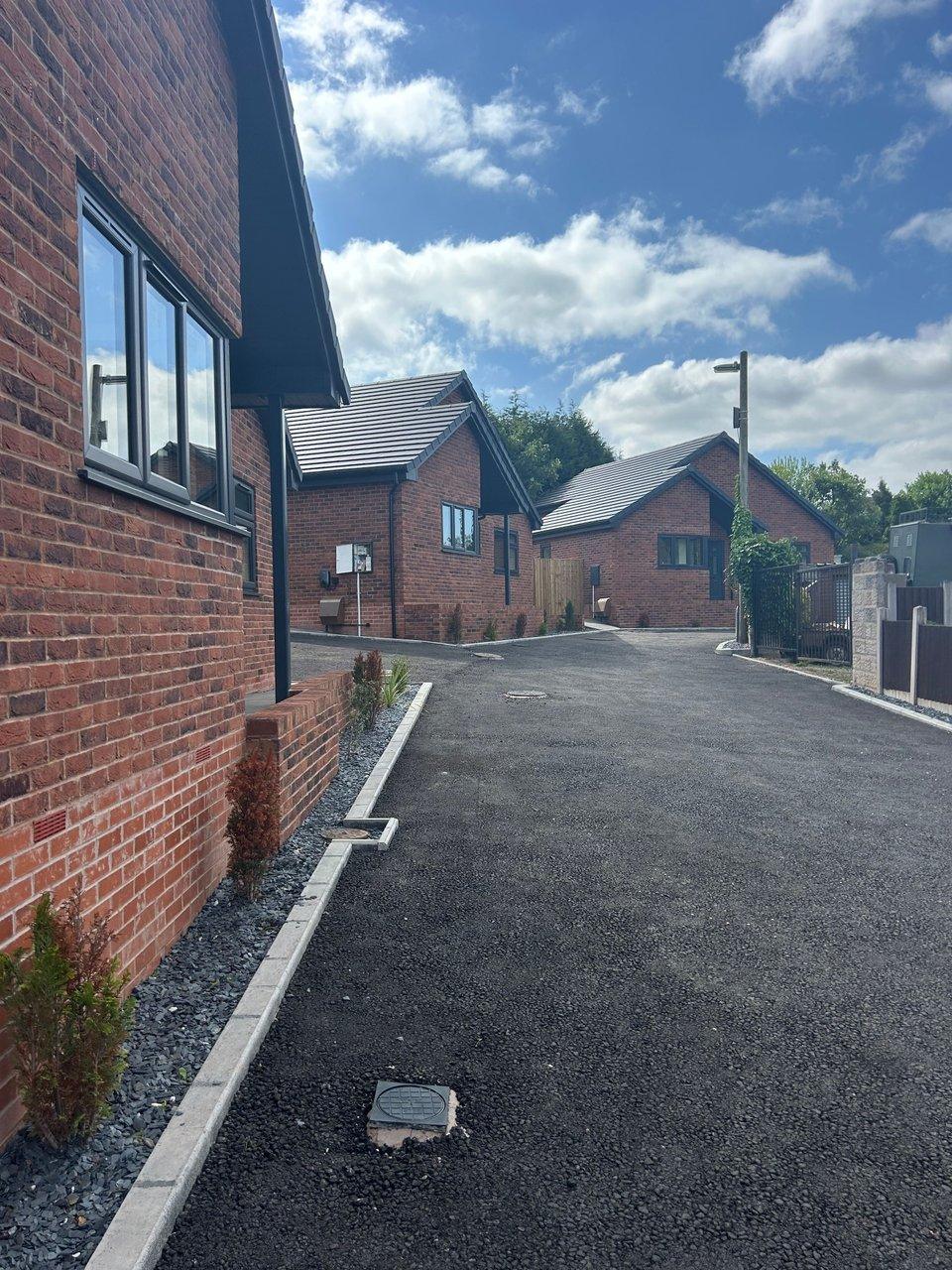 New red-brick houses beside a freshly paved driveway under a blue sky with clouds.