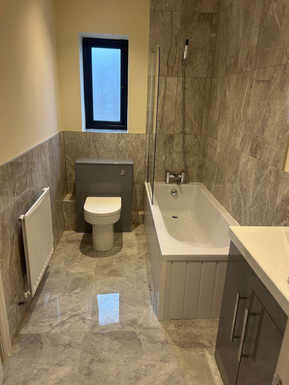 Bathroom with a bathtub shower, toilet, vanity, radiator and narrow window.