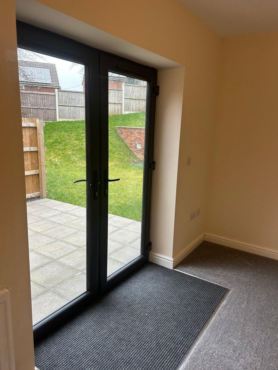 Black-framed glass patio doors opening onto a paved patio and grassy fenced garden.