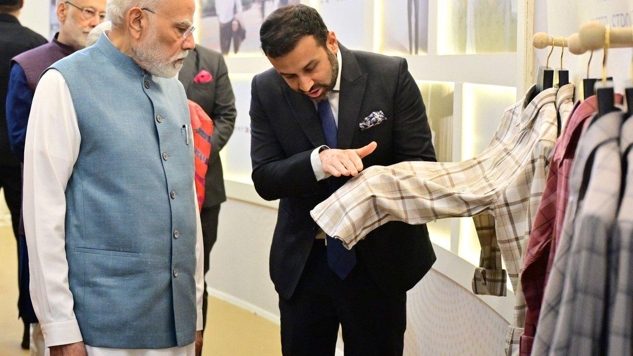Two men examine a beige plaid shirt on a clothing rack.