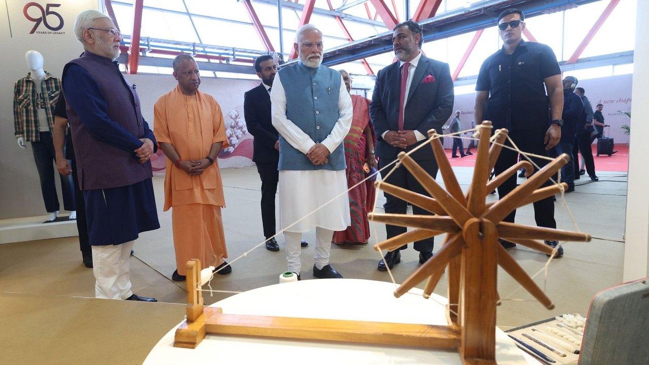 Several people examine a wooden spinning wheel display at an exhibition.