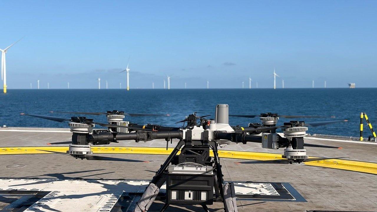 A large drone on an offshore platform helipad with wind turbines in the sea behind it