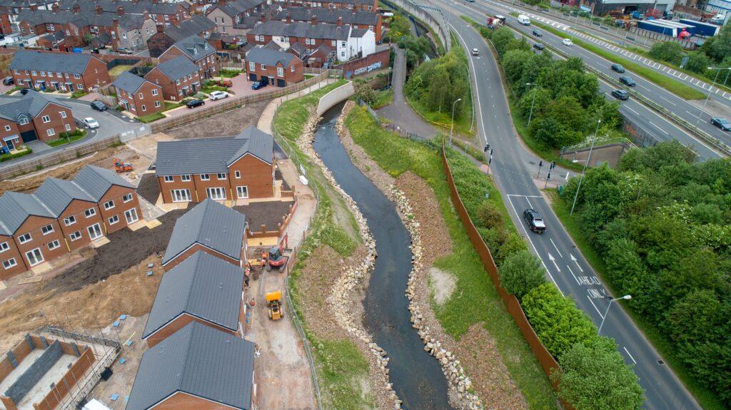 A newly restored river channel runs beside houses and a main road.