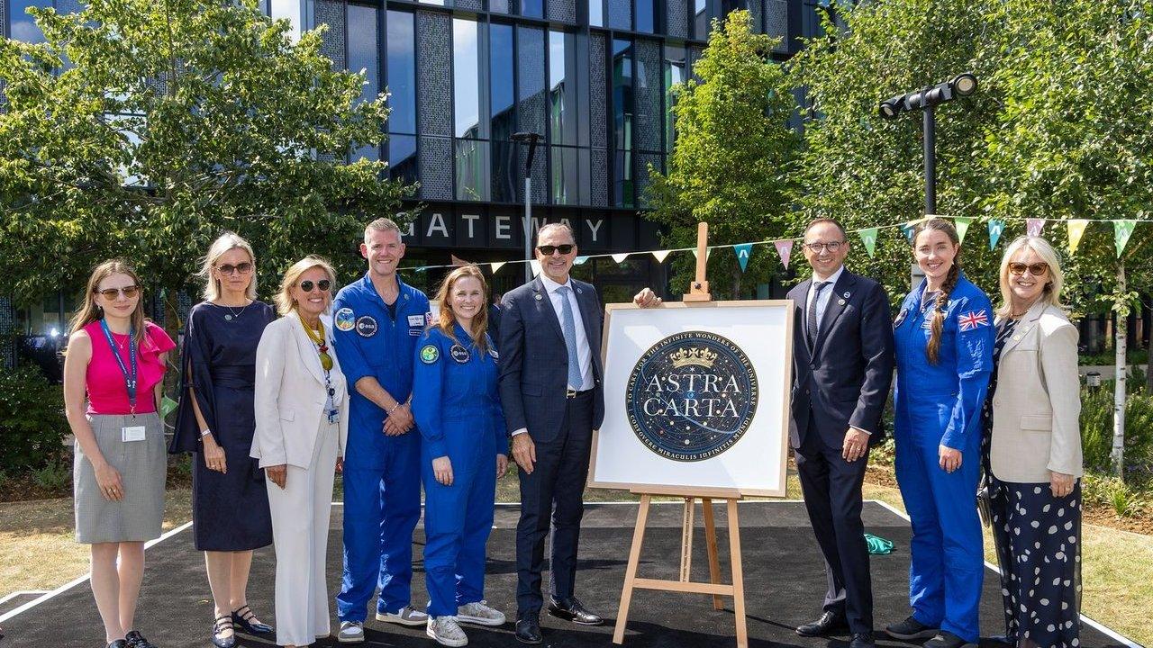 European Space Agency astronauts and guests beside an Astra Carta emblem on an easel outdoors
