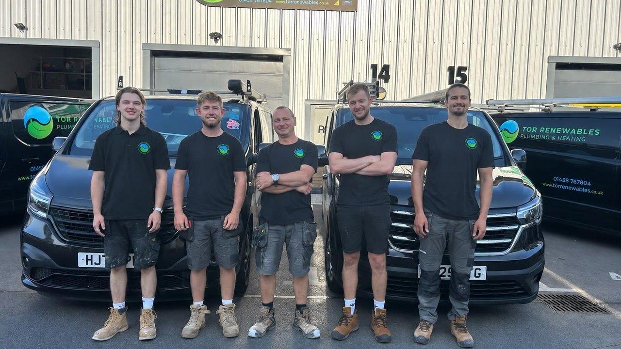 Five workers in Tor Renewables uniforms stand in front of branded company vans.