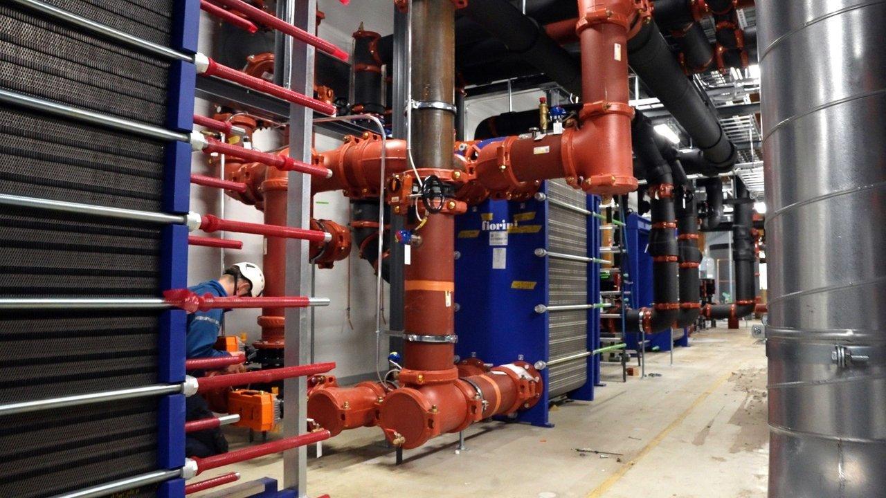 Industrial heat recovery equipment with red pipes, blue heat exchangers and a worker in a hard hat.