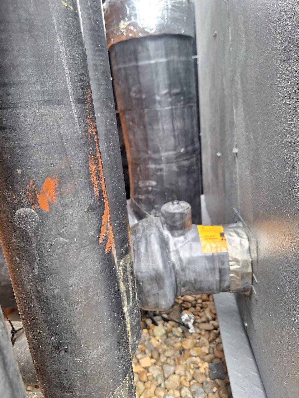 Insulated heat pump pipes and a valve connection on a gravel-covered roof.