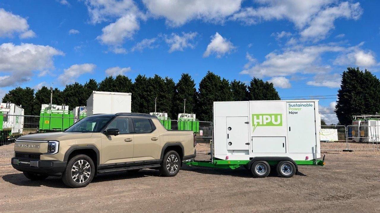 A beige pickup truck towing a white and green mobile power unit trailer.