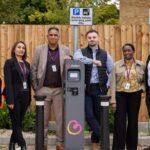 Six employees stand beside a Believ electric vehicle charging point.