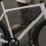 A person standing beside a gray Lemmo electric bicycle with black fenders and a frame-mounted battery.