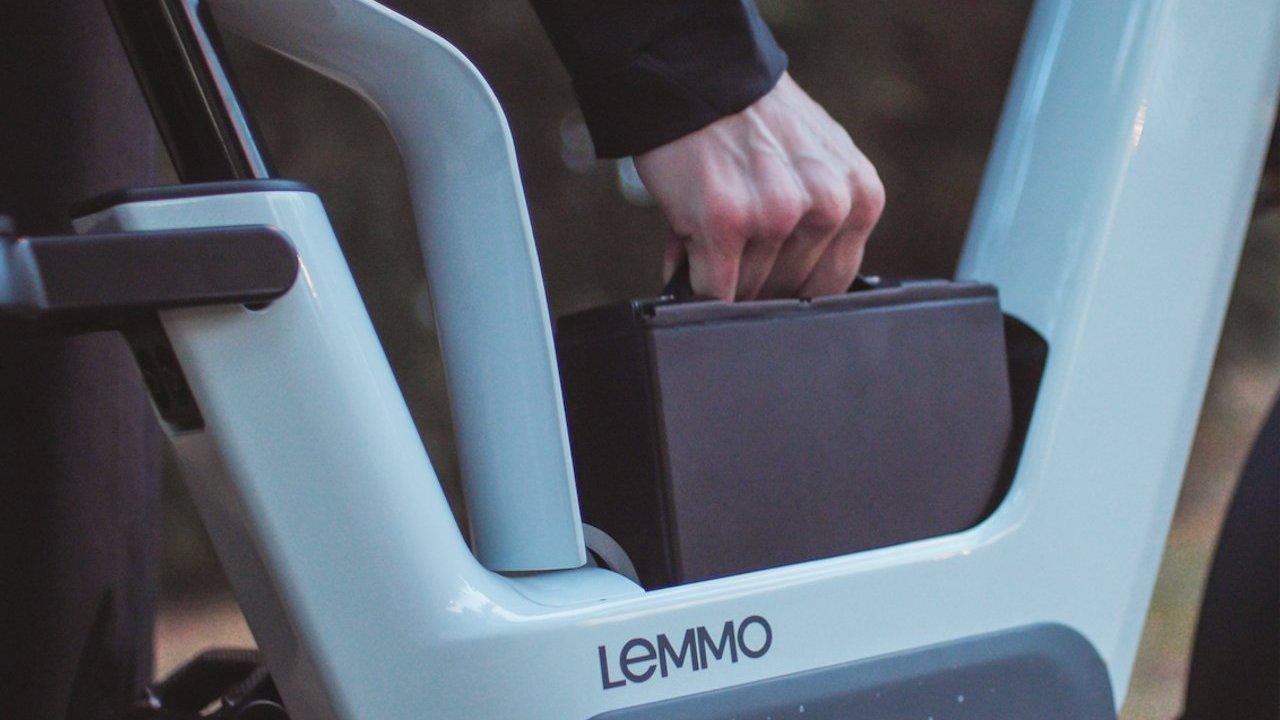 A hand places a black briefcase in the frame of a Lemmo electric bicycle.
