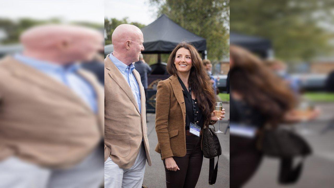 A woman holding a champagne flute talks with a man at an outdoor event.