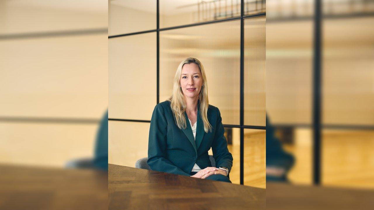 Marjella Lecourt Alma seated at a table in an office, wearing a dark teal blazer.
