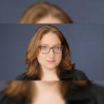 Rebecca Brocato wearing glasses and a black jacket against a blue-gray background.