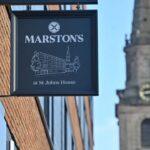 Marston’s at St Johns House sign on a brick building with a church clock tower behind