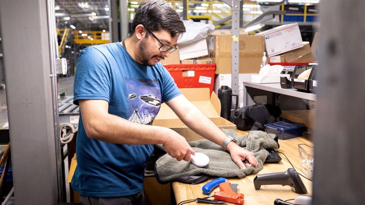 A man brushes a gray towel at a workbench in a warehouse.