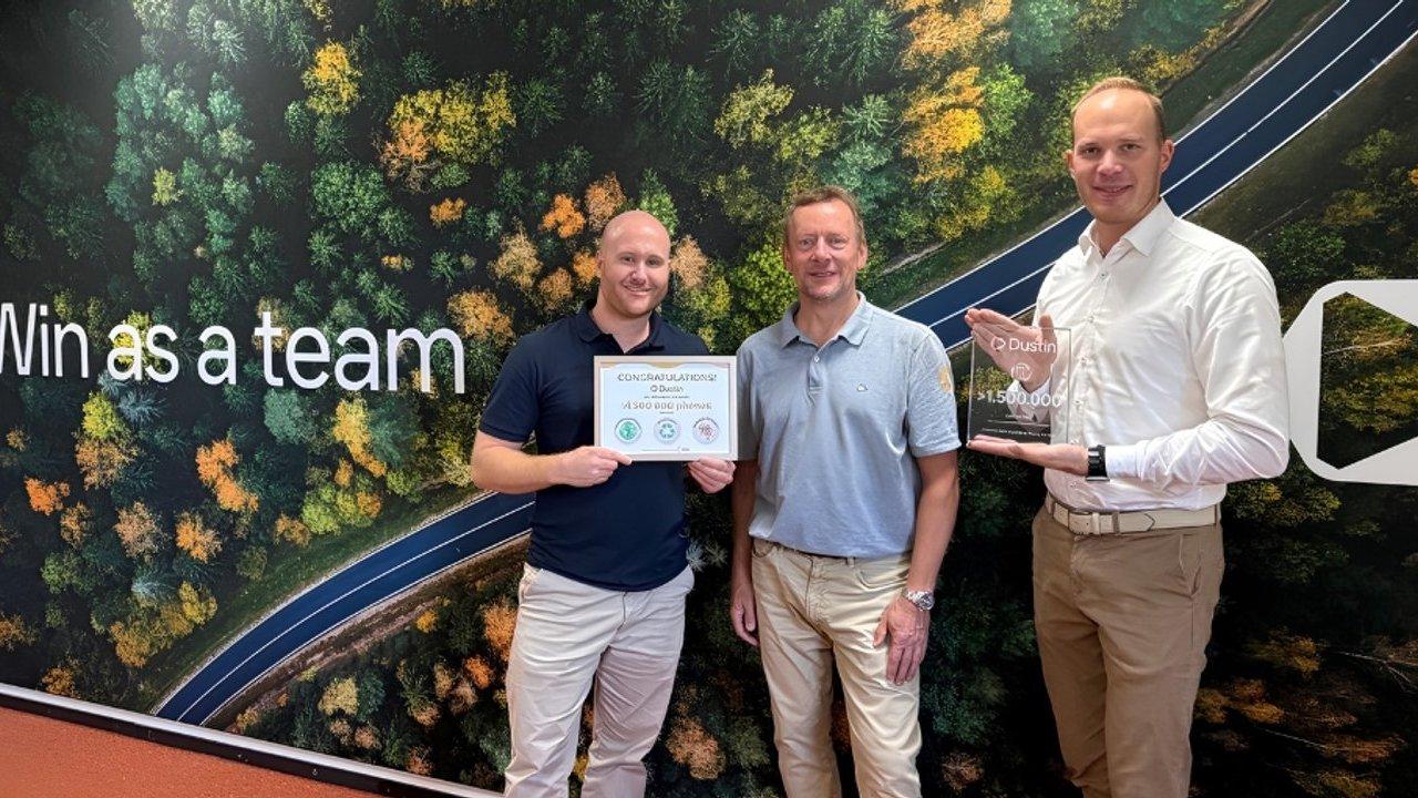 Three men hold a diploma certificate and a €1,500 award plaque before a forest road mural.