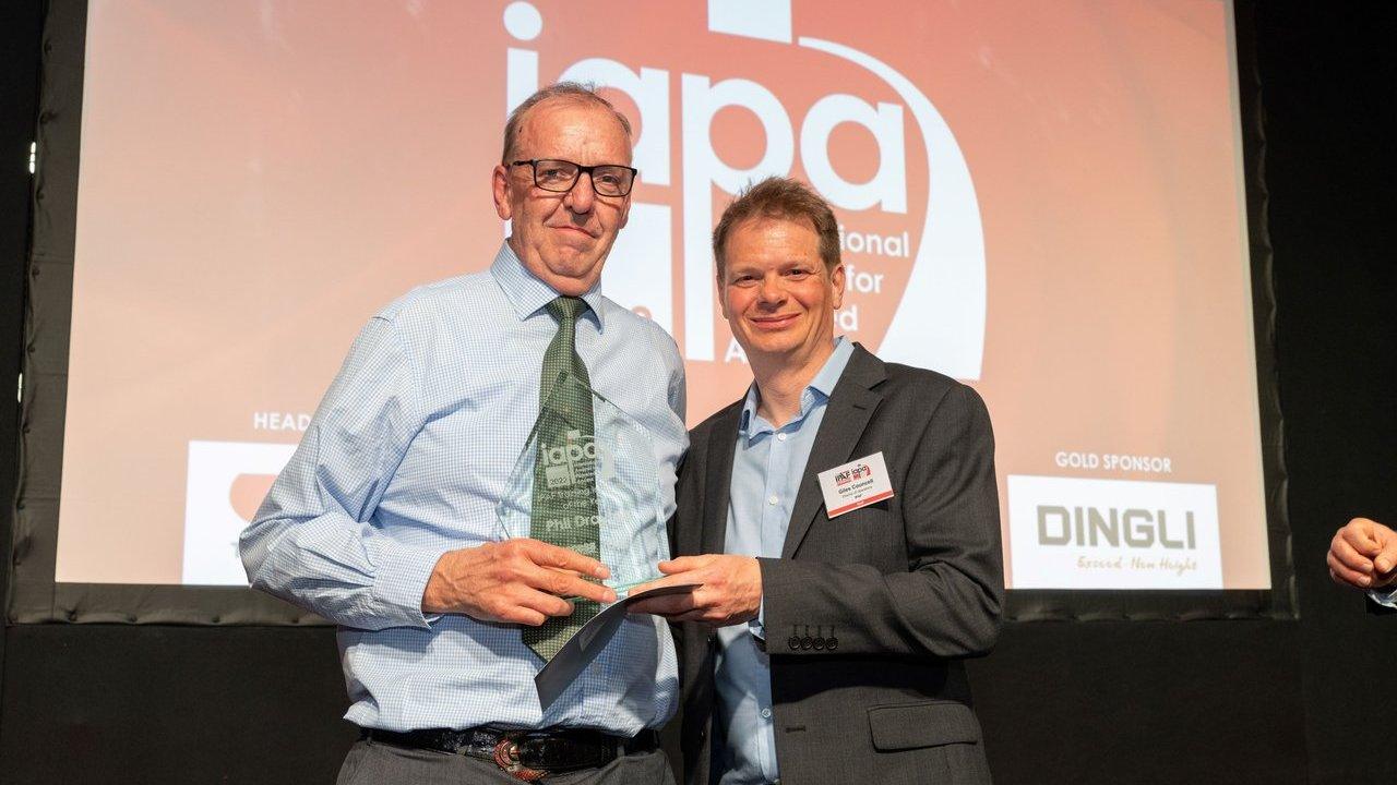 Two men holding an award trophy onstage in front of a presentation screen.
