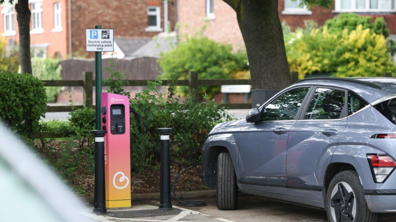 A grey electric car parked beside a pink and yellow vehicle charging station.