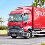 A red Symphony delivery truck on a tree-lined road.