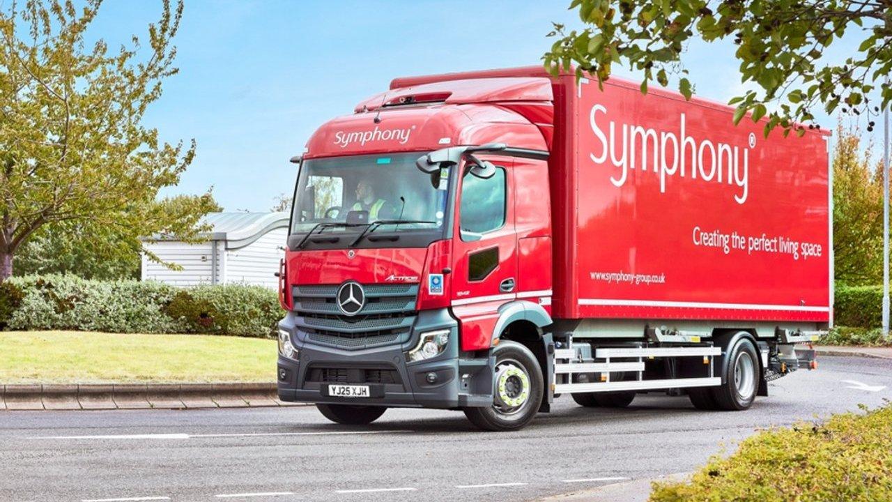 A red Symphony delivery truck on a tree-lined road.