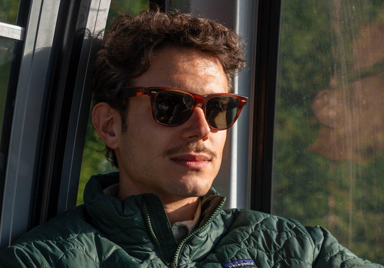 A man in sunglasses wearing a dark green quilted Patagonia Heyes Peak jacket, seated by a window