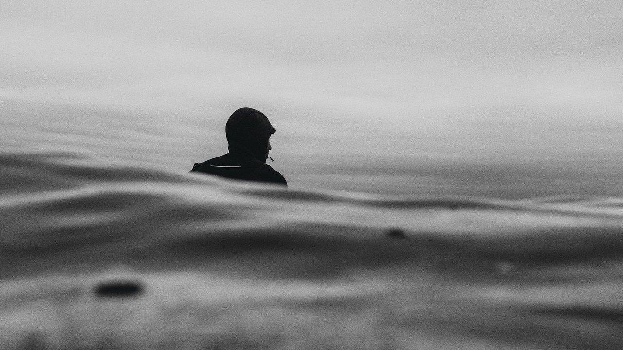 Silhouette of a helmeted surfer floating in ocean waves under a cloudy sky