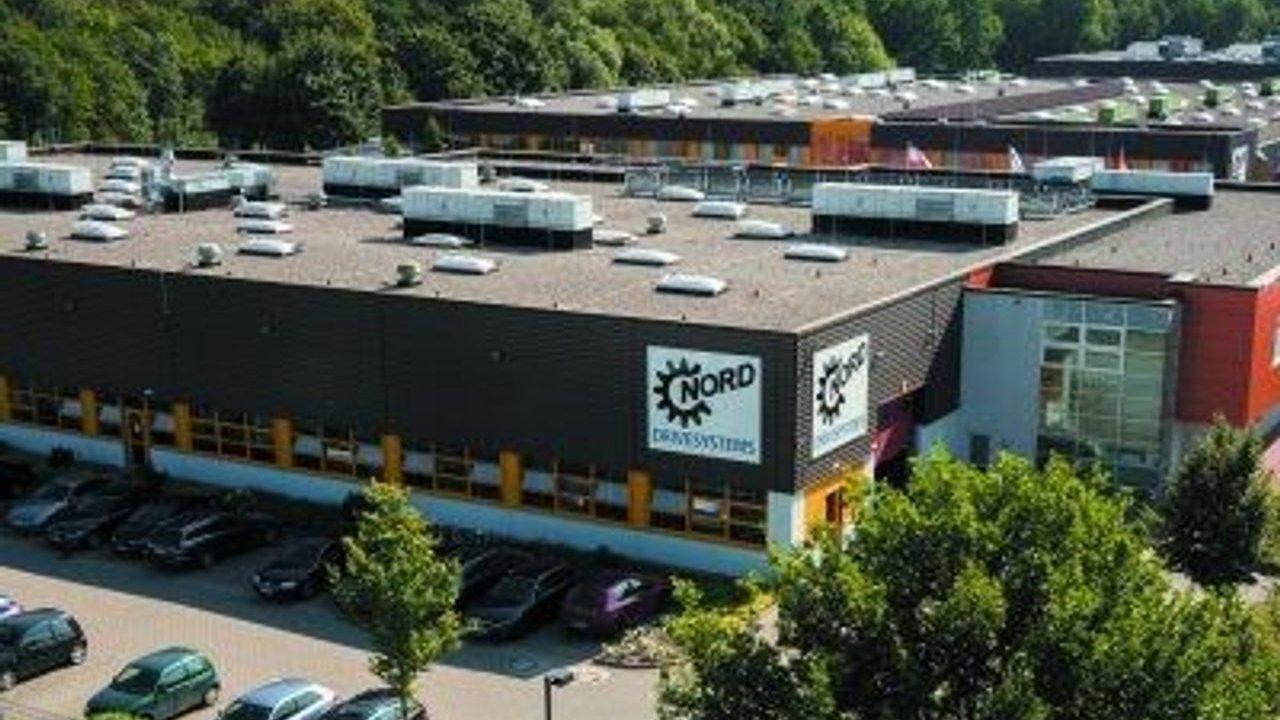 A Nord Furniture store building with parked cars, rooftop units and surrounding trees