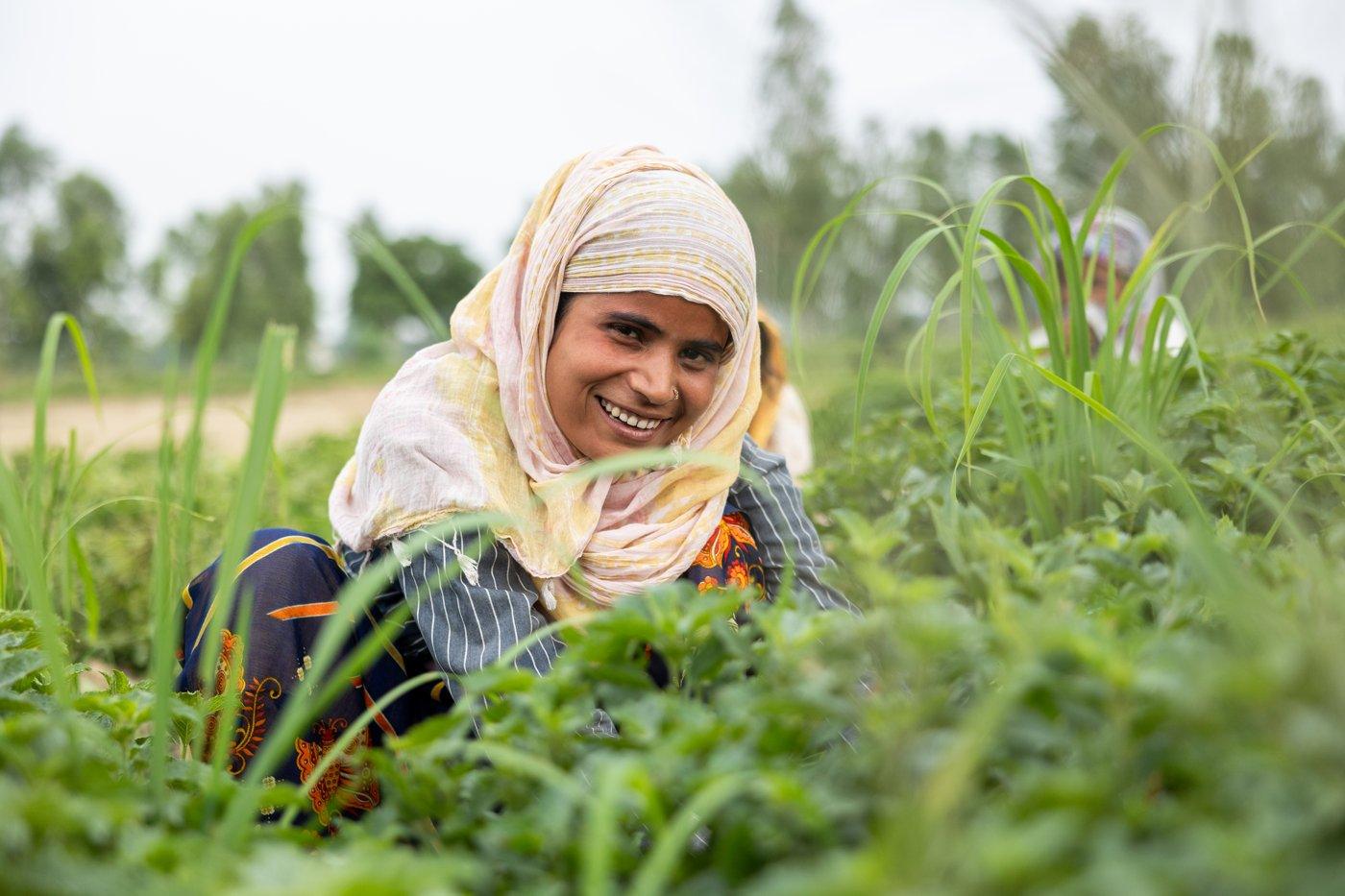 A smiling woman in a headscarf among mint plants in a field