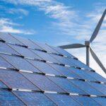 Solar panels beside a wind turbine under a blue, partly cloudy sky.