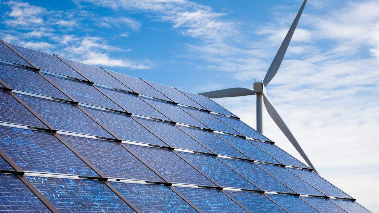 Solar panels beside a wind turbine under a blue, partly cloudy sky.