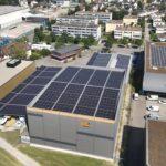 Industrial buildings with rooftop solar panels beside a residential neighborhood.